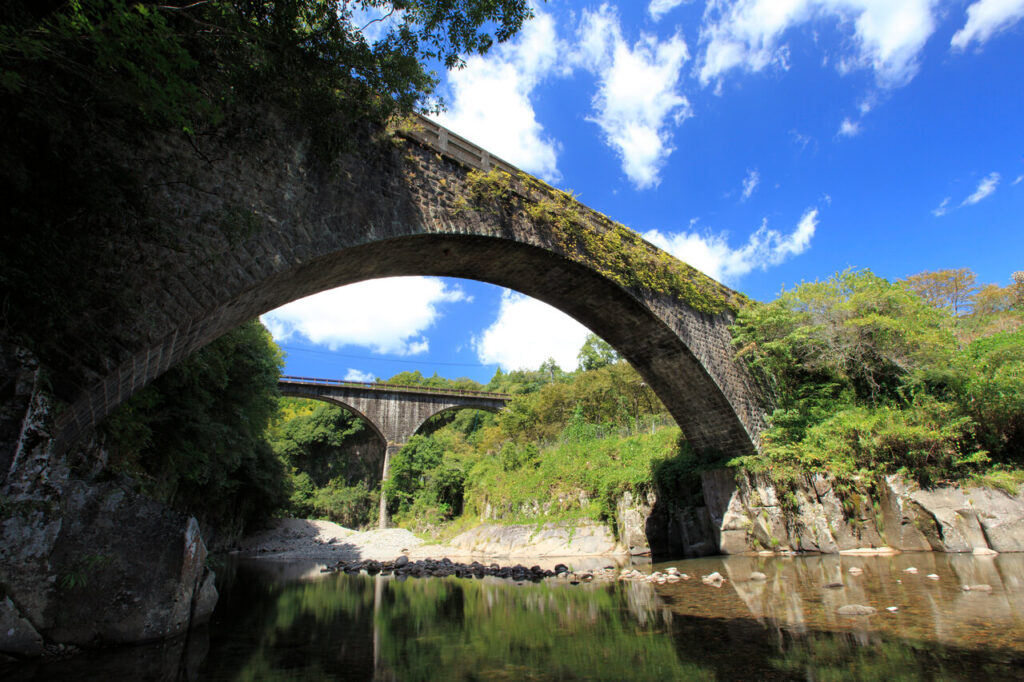 奥嶽川の渓谷に架かるアーチ式石橋を下から望む。青空と清流、緑に囲まれた美しい景観