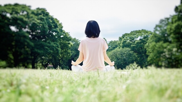 旅庵 蕗薹の体験イメージ、森に向かって草原に座り座禅を行う女性の後ろ姿