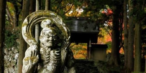 両子寺の参道に立つ苔むした仁王石像と、背後を彩る紅葉