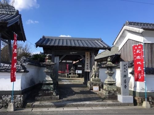 興満山興導寺の山門。両脇に火燃地蔵尊の赤い幟と石灯籠・石仏が並ぶ
