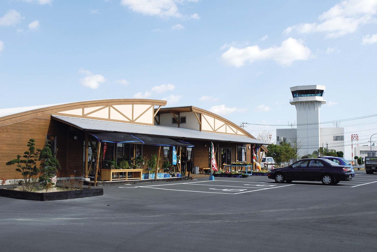 大分の空 むさし（里の駅 大分の空武蔵）の全景。アーチ屋根の建物と広い駐車場、背景に大分空港の管制塔と青空