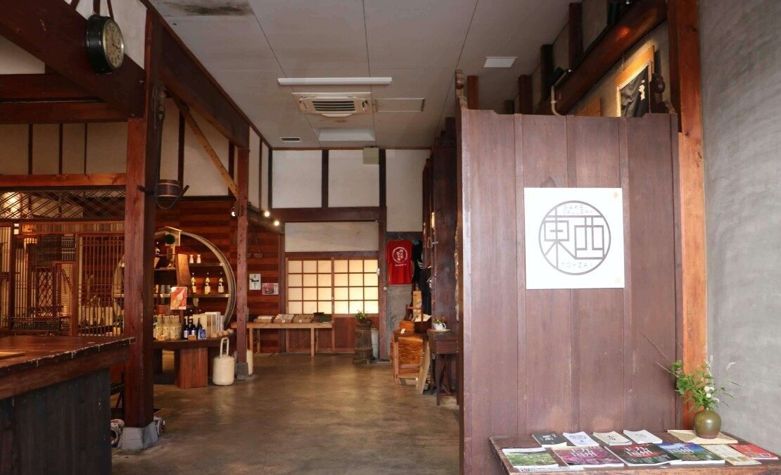 サケギャラリー東西の店内奥。木の仕切りに「東西」の屋号マークが掲げられ、商品の陳列棚が広がる