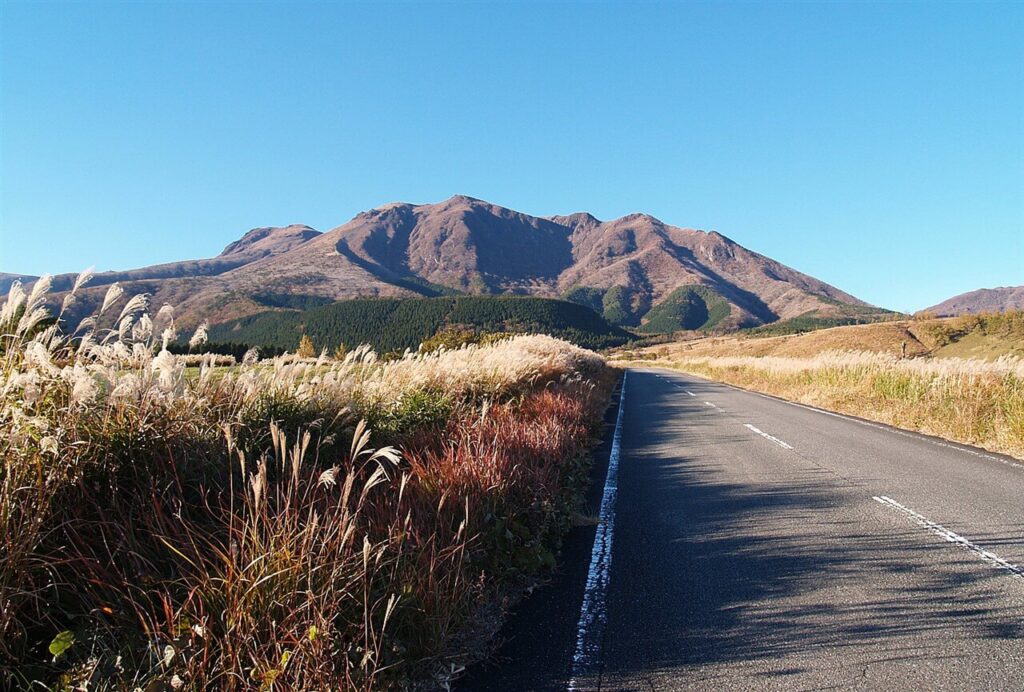 秋の絶景ドライブにおすすめな、ススキが揺れる一本道の向こうにくじゅう連山を望む久住高原の道路