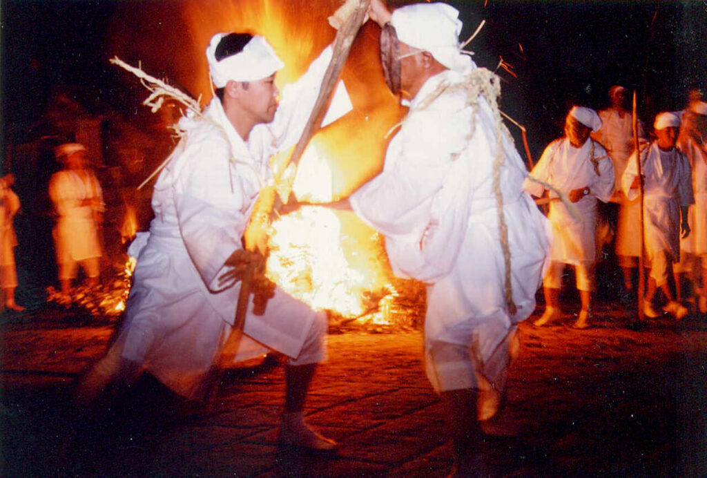 ケベス祭で炎を背に向き合う白装束の二人｜櫛来社