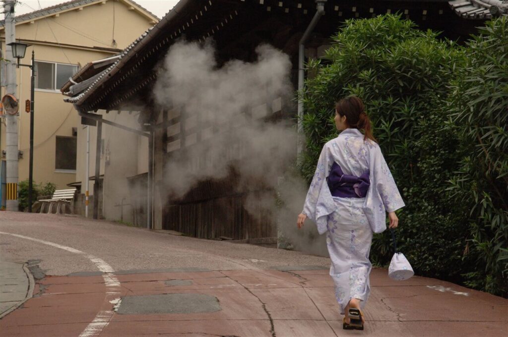 雨の鉄輪温泉を浴衣で歩く女性。湯けむりが漂う別府の情緒ある風景（いでゆ坂）