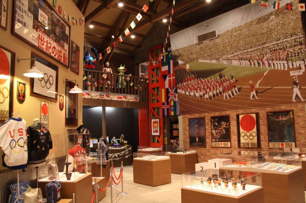 昭和ロマン蔵の室内展示、1964年東京オリンピック開会式の選手入場の写真が壁一面に飾られ、五輪マークや当時の国旗も展示された様子