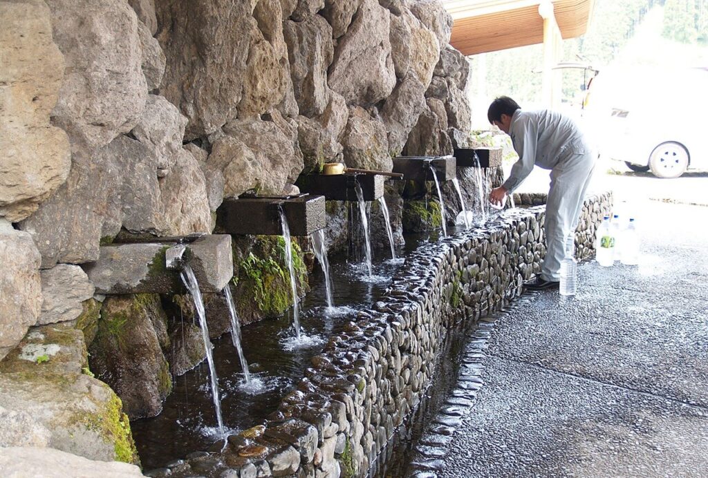 たくさんの蛇口から名水が勢いよく流れ出る、小津留湧水（水の駅おづる）で水を汲む男性の様子