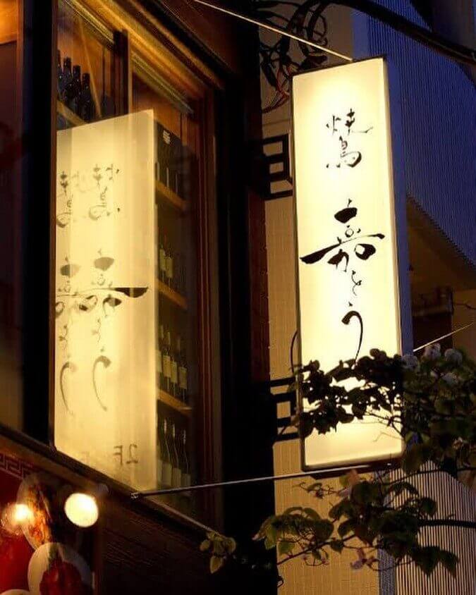 東京都にある地鶏の店「焼鳥　嘉とう」店前で明かりのついた看板を下から撮影