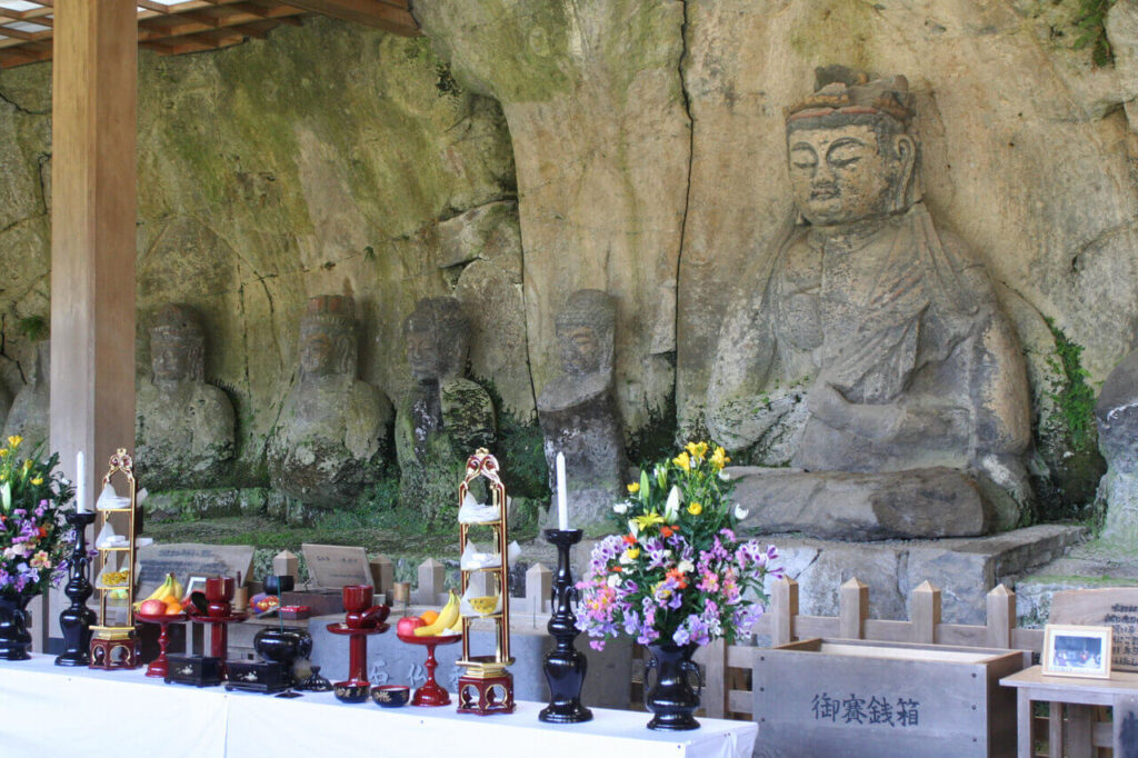 臼杵石仏 古園石仏前の供物と賽銭箱 左に並ぶ石仏群の全景（大分県臼杵市）