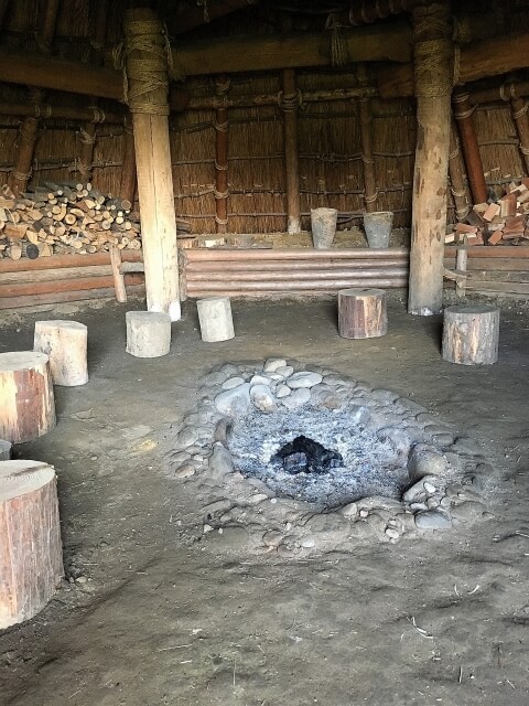 囲炉裏を中心に木製の腰掛けが配置された弥生時代の竪穴式住居内部