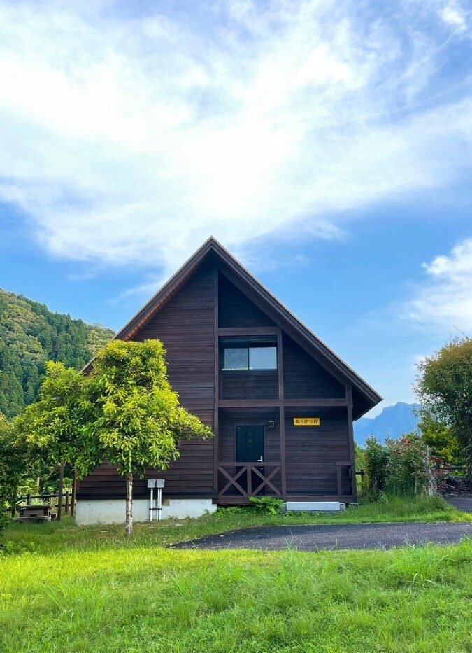 山並みを背景に建つロフト付きケビン「おうけつ谷」外観。前面に緑豊かな木々
